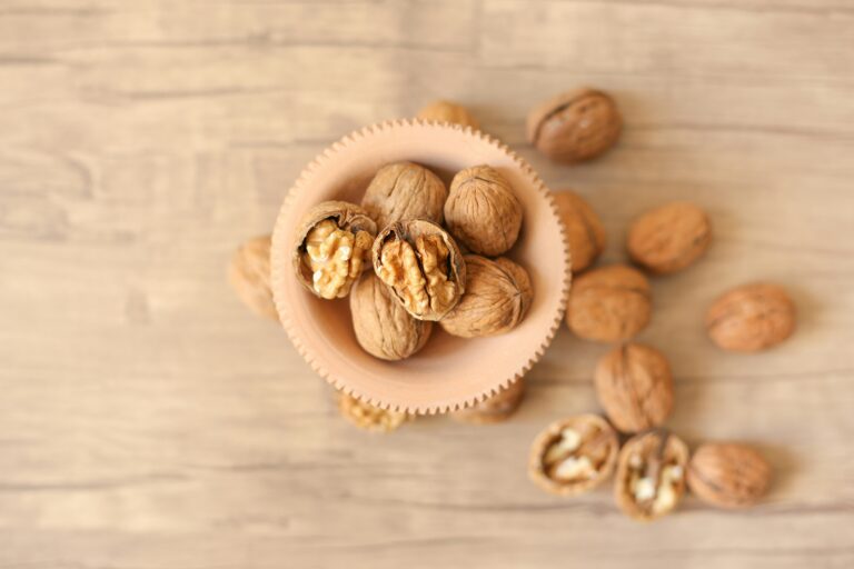 Wooden background with some walnuts in a bowl and some outside the bowl