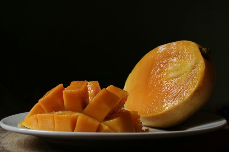 A plate of peeled mango cubes and half a peeled mango on a table