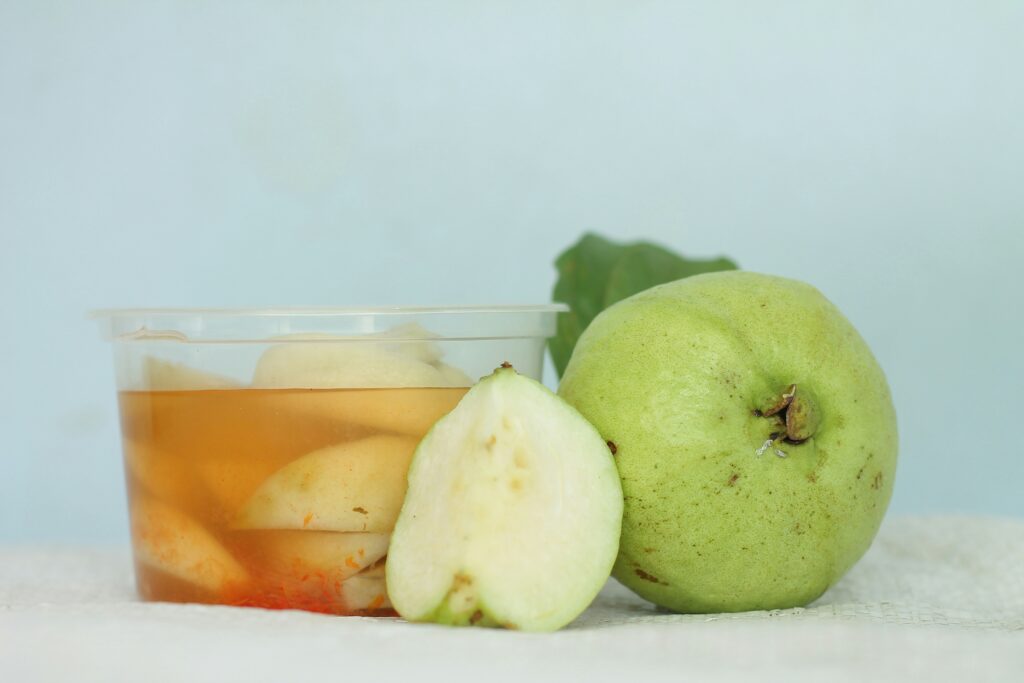One whole and one slice of guava placed in front of a small container filled with liquid and spices, with the remaining three slices of guava positioned behind it.