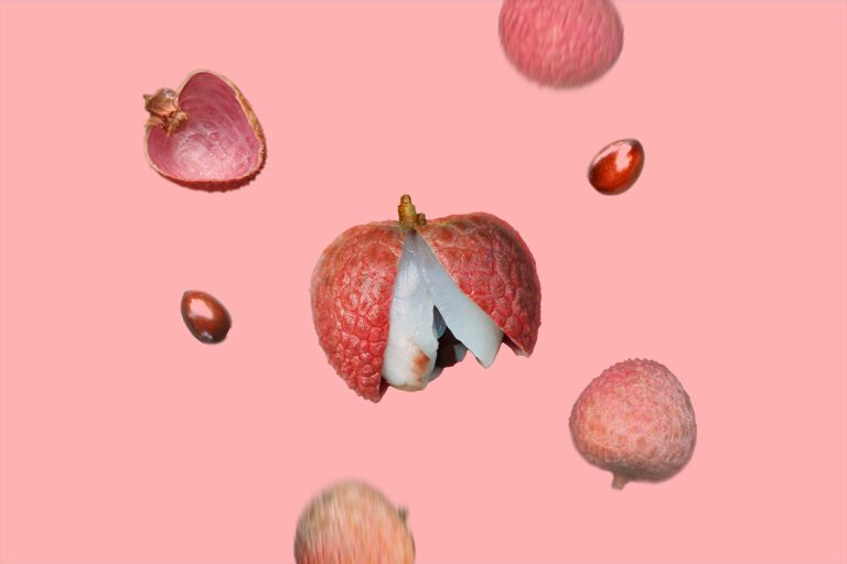 Lychees falling against a dark pink background, with one lychee in the center in sharp focus, partially peeled to reveal its translucent flesh.